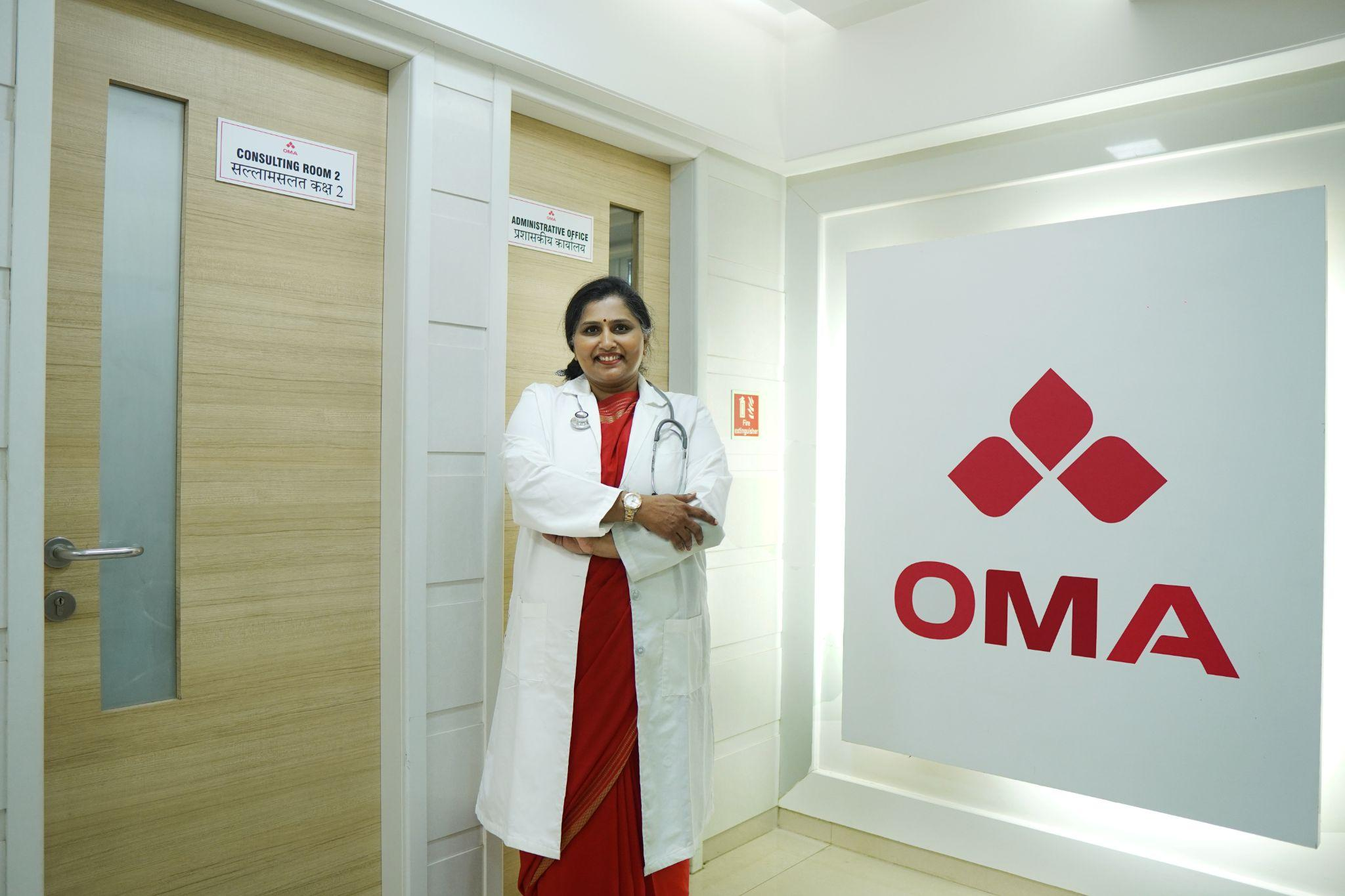 Picture1(81) Smiling female doctor in a white coat with a stethoscope stands in a hospital corridor beside doors labeled Consulting Room 2 and Administrative Office.